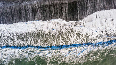 Amazing picturesque view of black sand beach with wave of Reynisfjara in Iceland. Aereal winter landscape view of Reynisfjara from drone. Black sand beach under snow at winter time.の写真素材