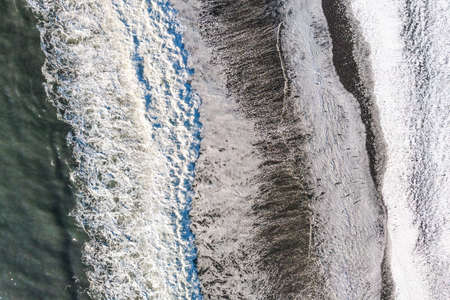 Amazing picturesque view of black sand beach with wave of Reynisfjara in Iceland. Aereal winter landscape view of Reynisfjara from drone. Black sand beach under snow at winter time.の写真素材