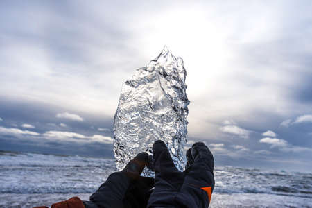 Male hand holds a large piece of ice on Diamond beach near Jokulsarlon lagoon in winter time, Iceland.の写真素材