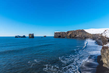 Aerial winter landscape view of Dyrholaey, Iceland. Beautiful winter view of picturesque peninsula with black sand beach, lighthouse and large arch of volcanic rocks in the ocean.の写真素材