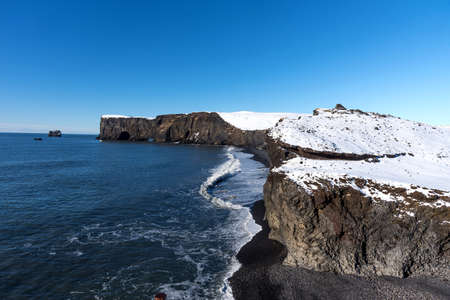 Aerial winter landscape view of Dyrholaey, Iceland. Beautiful winter view of picturesque peninsula with black sand beach, lighthouse and large arch of volcanic rocks in the ocean.の写真素材