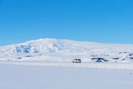 Beautiful winter landscape with mountains covered snow, cold frosty weather and asphalt road through a white field in Iceland.の写真素材