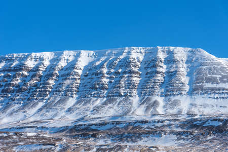 Beautiful winter landscape with mountains covered snow, cold frosty weather and asphalt road through a white field in Iceland.の写真素材