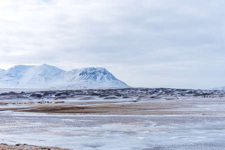 Beautiful winter landscape with mountains covered snow, cold frosty weather and asphalt road through a white field in Iceland.の写真素材