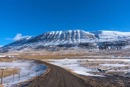 Beautiful winter landscape with mountains covered snow, cold frosty weather and asphalt road through a white field in Iceland.の写真素材