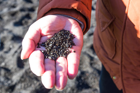 Black sand on the white man hand on the background of famous black sand beach Reynisfjara in Iceland. Close up black volcanic sand in man hand.の写真素材