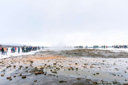 Tourists stand around Strokkur and wait the eruption in Iceland. Eruption of Strokkur a fountain geyser located in the Haukadalur geothermal area, southwest of Iceland. Haukadalur is part of the Goldeの写真素材