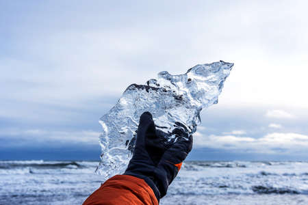 Male hand holds a large piece of ice on Diamond beach near Jokulsarlon lagoon in winter time, Iceland.の写真素材