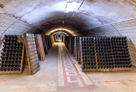 Abrau-Durso, Russia - March 2, 2021: Champagne and sparkling wine factory Abrau Durso in Russia. Stack of wine bottles in old dark wine cellar.のeditorial素材