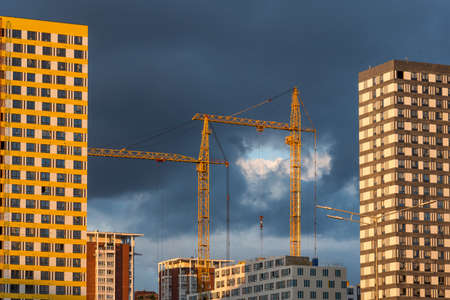 Working crane on a modern residential building under construction against dramatic sky in Russia. Residential complex under construction with high cranes. Residential building construction.の写真素材