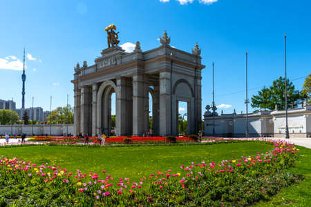 Moscow, Russia - June 2, 2022: Arch of the main entrance of VDNKh. In front of the arch flower beds with red and yellow tulips.のeditorial素材