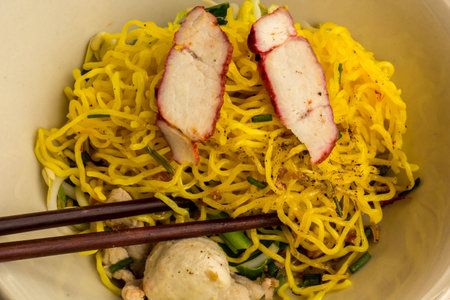 Yellow noodles, a bowl of pork dishes, chopsticks cilantro.