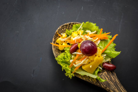 Fresh spring salad with rucola, feta cheese, red onion and pomegranate seeds in black bowl on chalkboard background with free text space.の写真素材