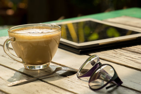 Black coffee with blank digital tablet and mobile phone, magazines and glasses on the table. Break conceptの写真素材
