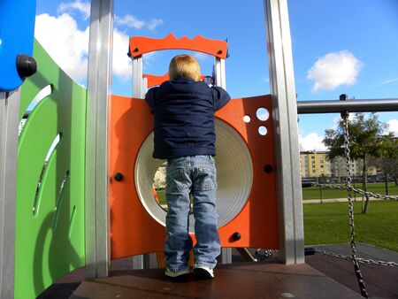 Little boy rear view in the park on the playground stands near the tunnel pipeの写真素材