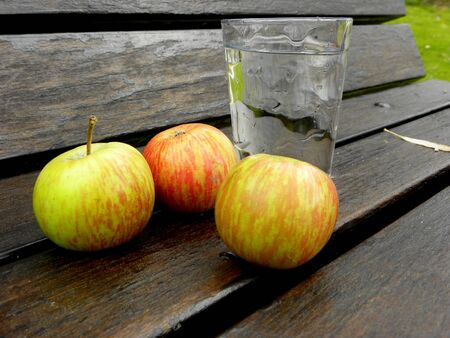 three ripe red-yellow apples and a glass of waterの写真素材