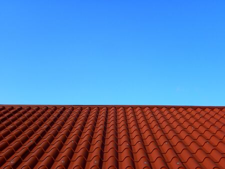 Red tile roof under blue sky. The photo is divided in half. One part is a roof made of clay tiles and the other is a pure blue sky.の素材 [FY310141922648]