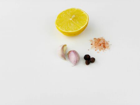 half ripe lemon, two cloves of garlic, grains of pepper and pink salt on a white backgroundの写真素材
