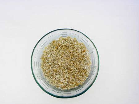 Soaking pearl barley in a water to ferment cereals and neutralize phytic acid. Large glass bowl with grains flooded with water. Top view, close up, white backgroundの写真素材