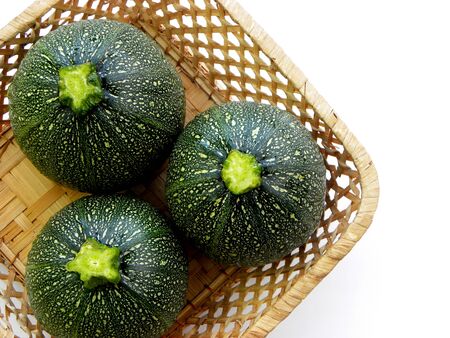 three green round zucchini close-up in a wicker basket on a white backgroundの写真素材