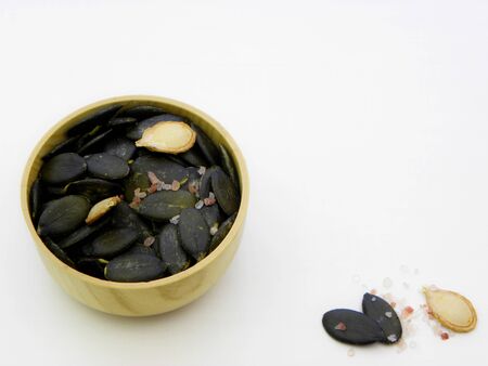 Pumpkin seeds with salt. Peeled pumpkin seeds in a wooden bowl close-up on a white background.の写真素材