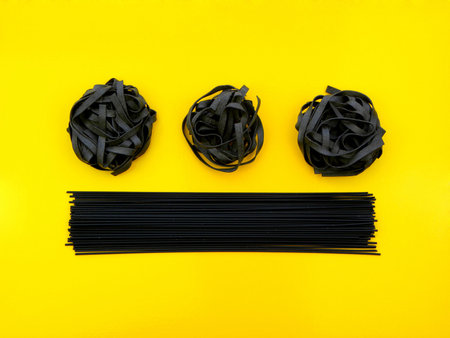 Tagliatelle and linguine pasta with cuttlefish ink on a yellow background.の写真素材