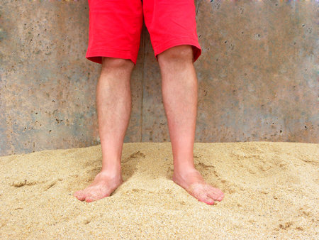 Male feet in the sand. Legs of a man in red shorts. Male feet on the yellow sand of Ericeira beach,...