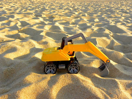 Yellow plastic excavator in the sand. Toy construction equipment. Children's toys on the beach.の写真素材