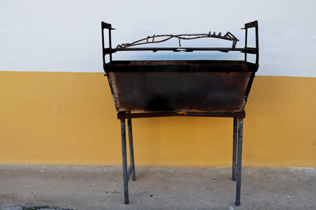 Old grill without coals on the background of a yellow and white wall. An empty grill with no charcoal or meat.の写真素材