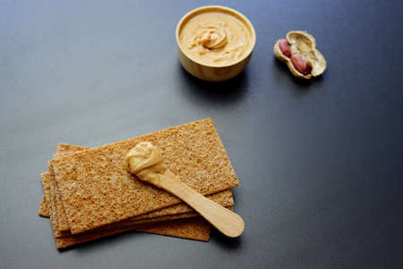 Peanut butter in a round wooden bowl and rye bread on a gray background.の写真素材