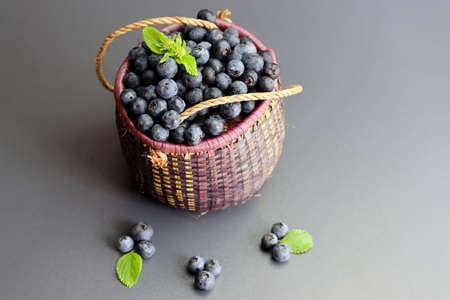 Blueberries with green leaves in a wicker basket on a gray background. Blueberry antioxidant. Healthy food and nutrition conceptの写真素材