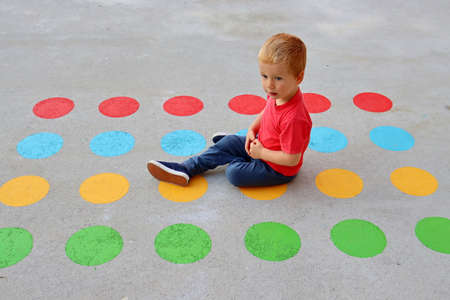 A blond boy sits on a floor painted with bright multi-colored circles. Portrait of a three-year-old charming boy.の写真素材
