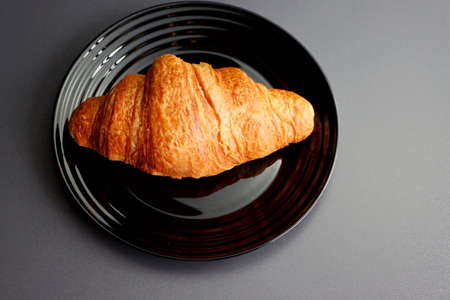 Ruddy croissant on a black plate on a gray background. Crescent-shaped croissant made of puff pastry. Croissant is a popular food in France.の写真素材