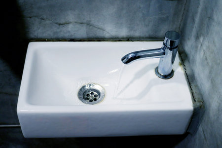 A small white washbasin in a washroom with gray walls. An old little sink.の写真素材