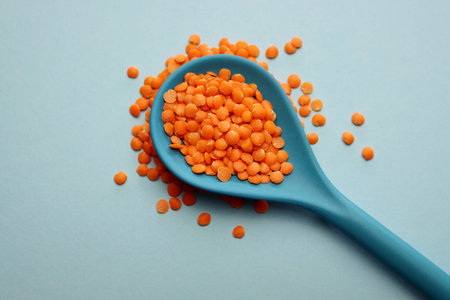 Red lentils in a blue bamboo spoon on a light blue background.
