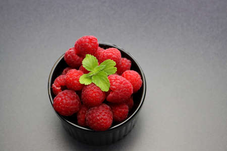 Fresh red raspberry and mint leaves in a black bowl on a gray background.の写真素材