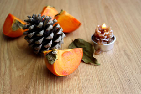 Slices of ripe orange persimmon on a wooden background. Autumn still life with orange fruit and fir cones.の写真素材