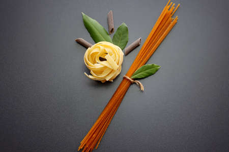 Tagliatelle pasta, brown penne rigate pasta, brown spaghetti and laurel leaves on a gray background.の写真素材