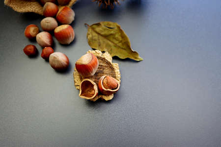 Peeled hazelnuts and shells on a wooden stand against a background of scattered nuts and autumn leavesの写真素材