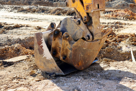 Three metal buckets of the excavator are lying neatly on the construction site among rocks and sand.