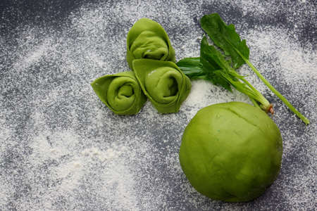 Raw homemade green tortellini, green dough and spinach leaves on a background of scattered flour.の写真素材