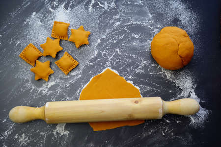 Raw orange ravioli in the form of rectangles and stars, dough and rolling pin on a background of scattered flour. The process of making homemade ravioli.の写真素材