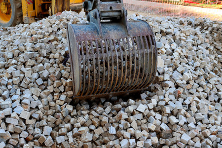 View of a excavator bucket and a pile of stones, close-up. Road repair construction.