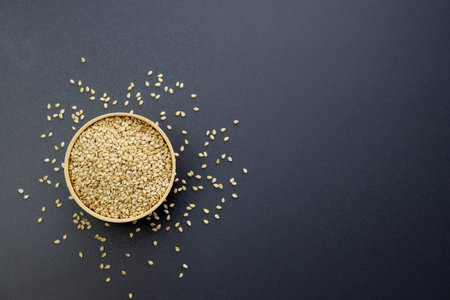 Sesame seeds in a round wooden bowl on a gray background.の写真素材