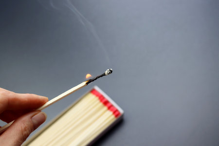 Burning match for the fireplace in a woman's hand on a gray backgroundの写真素材