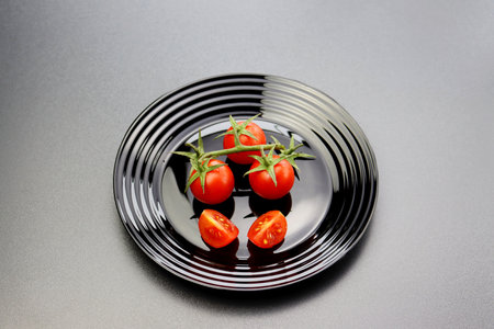 Red cherry tomatoes on a branch in a black plate on a gray background.の写真素材