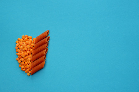 Red lentils and red penne pasta on a blue background. Red lentil penne paste.の写真素材