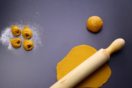 Raw homemade yellow tortellini, yellow dough and rolling pin on gray background. The process of making homemade tortellini.の写真素材