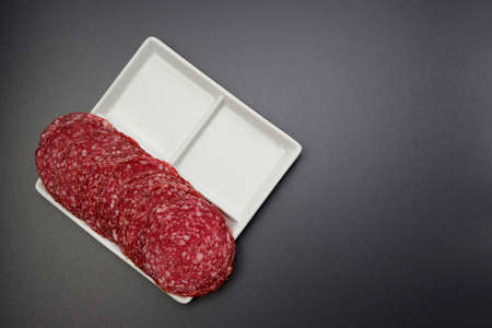 Appetizing round salami slices in a white square plate on a gray background.の写真素材