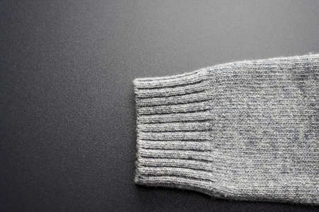 Part of a gray knitted wool sleeve on a gray background. Woolen knitted fabric texture.の写真素材